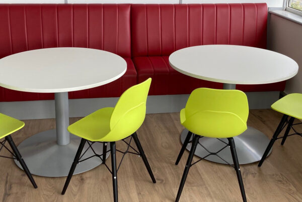 Office space planning implemented in this small canteen features soft seating benches, tables, and colourful canteen chairs