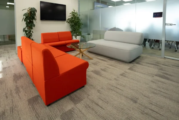 Office layout featuring a breakout space with soft seating around a table, and a glass walled meeting room in the background